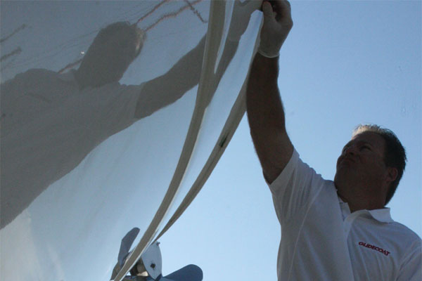 Man wearing white glove holding a sponge applying Glidecoat ceramic coating to the hull of a 1998 52' Princess