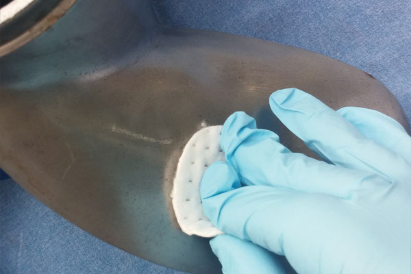 Blue glove with small fabric applying anti-fouling ceramic coating to a bronze prop blade