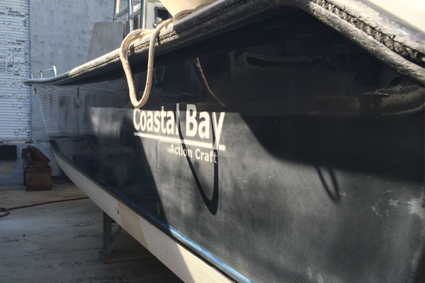 Port side of oxidized and faded black hull on Coastal Bay boat