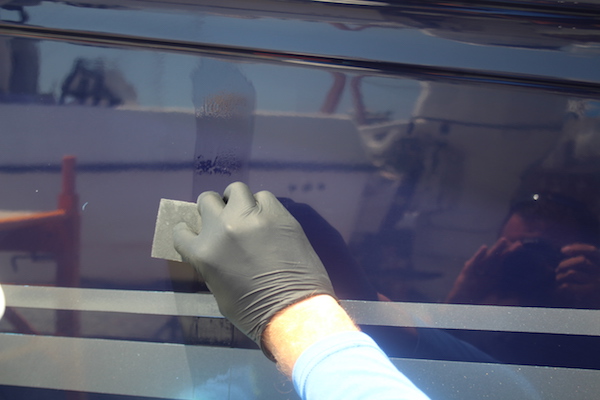 Man wearing black glove applying Glidecoat ceramic coating to the blue hull of a 32' Sea Ray Sundancer