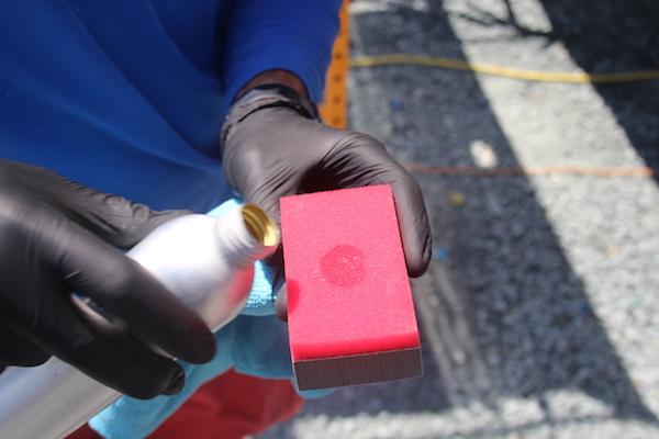 Man holding red sponge and silver bottle and a dime size of liquid ceramic coating poured into the middle of the sponge.