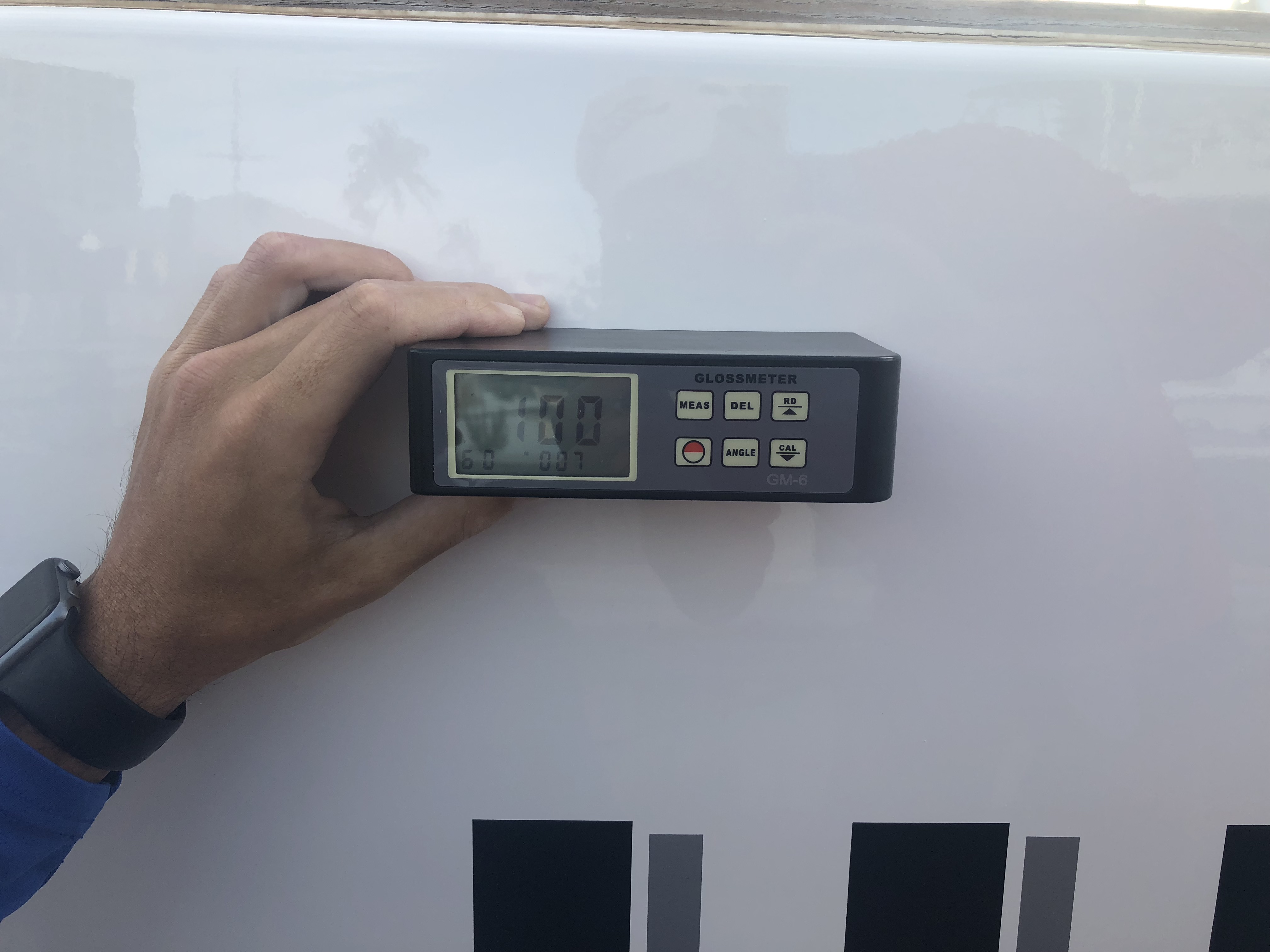 Man holding gloss meter with 100 reading on the transom of the 95' Heisley