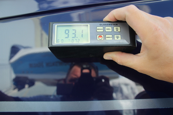Man taking photo holding gloss meter reading with 93.1 displaying on the screen