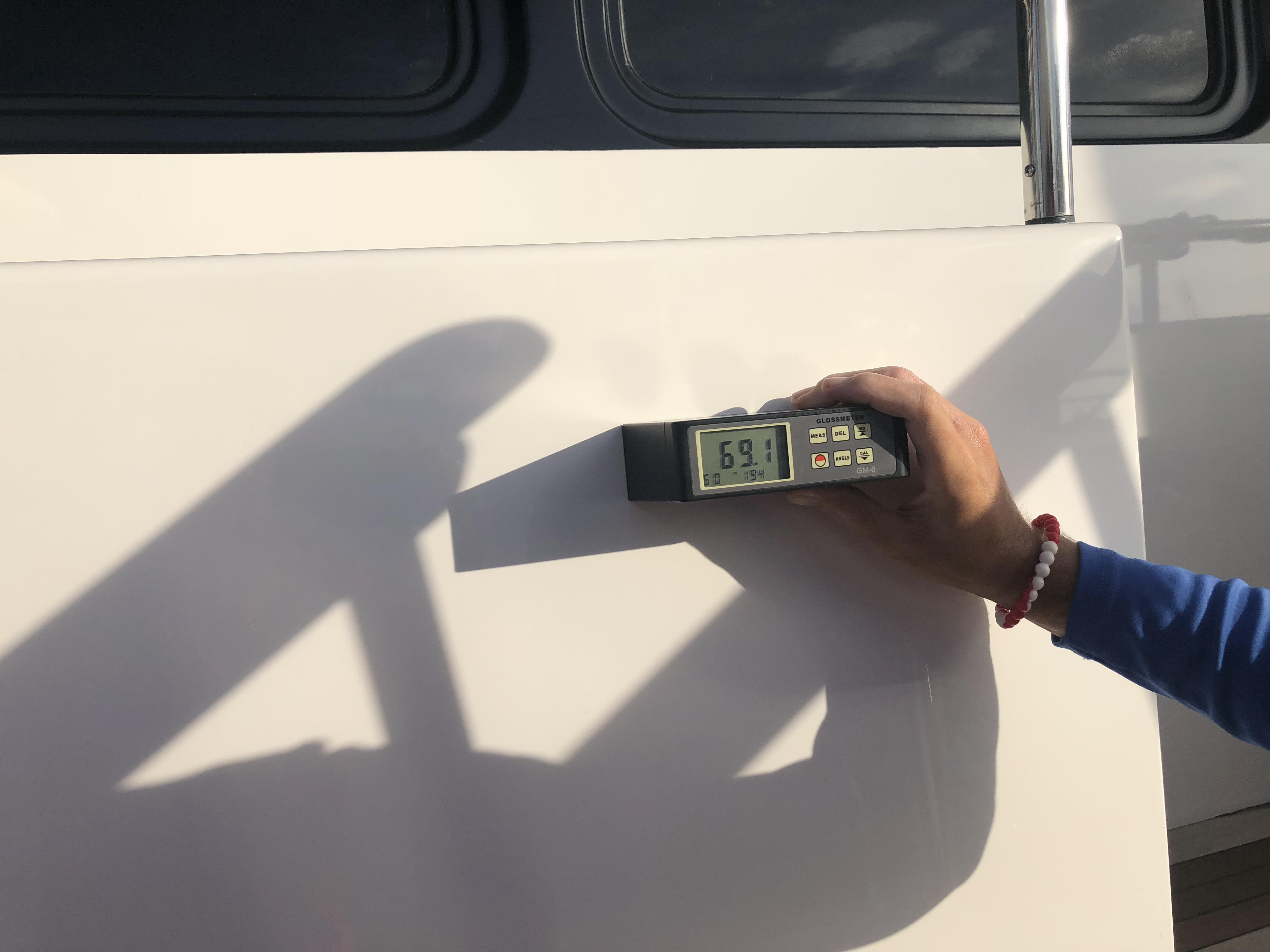 Man holding gloss meter reading on the hull of a Heisley reading 69.1