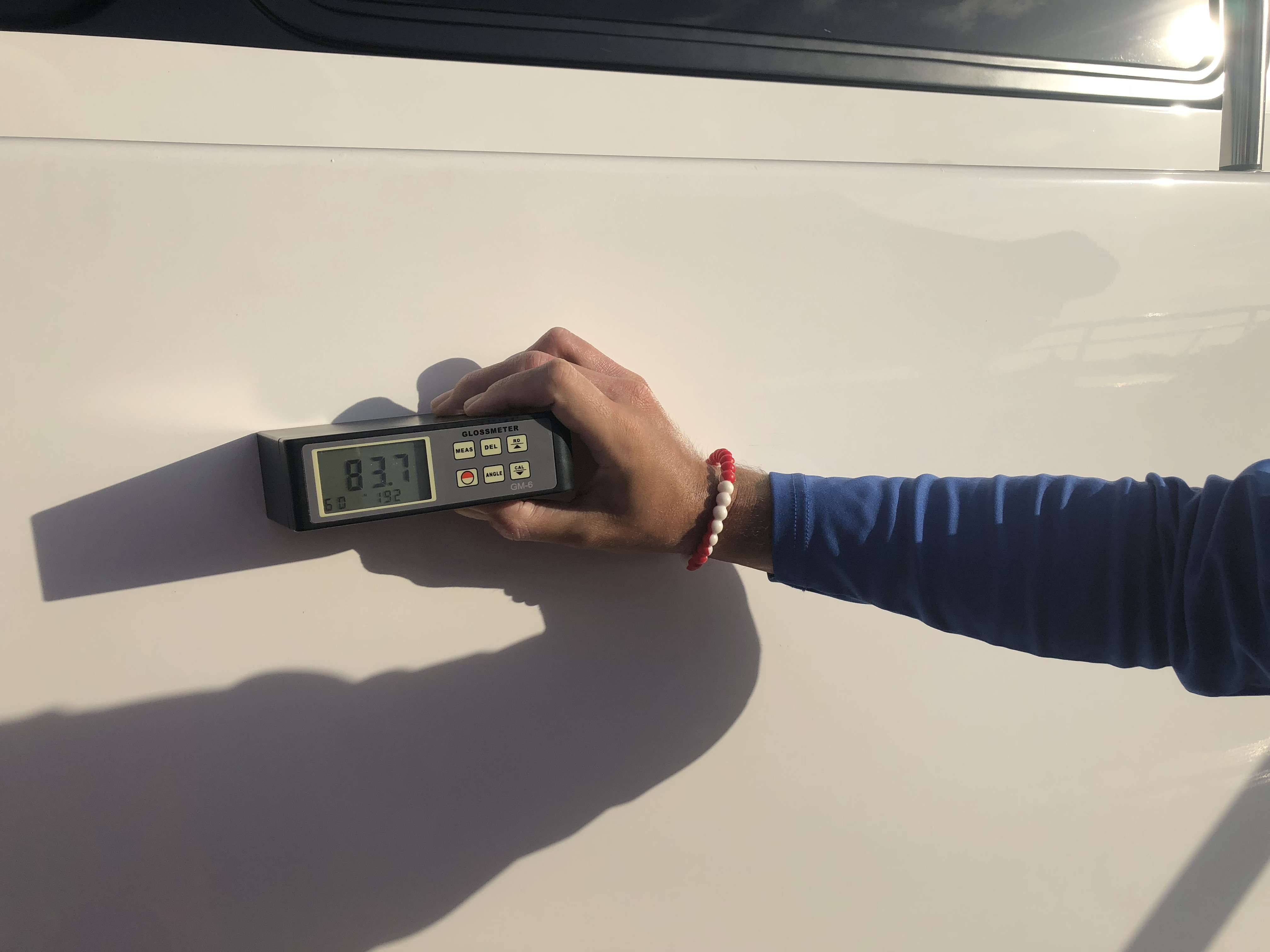 Man holding a gloss meter reading the reflection of the light on the white hull of a 95' Heisley. The gloss meter is reading 83.7